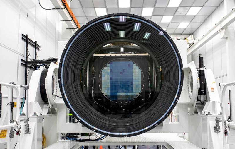 A digital camera sensor is visible through a large camera lens sitting inside a white room.