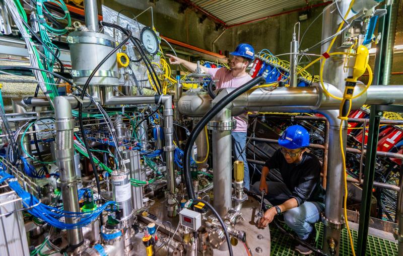 Two people in blue helmets examine experimental equipment.