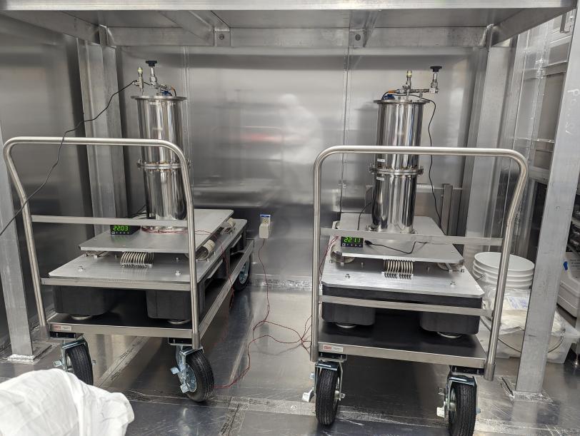 Two metal cylinders rest on carts in a metal room. 