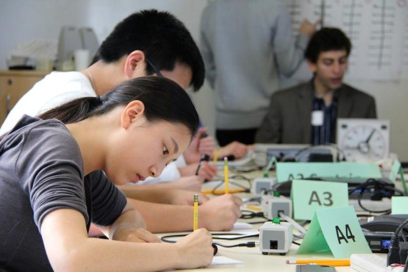 Photo - Close up of students writing at a table.