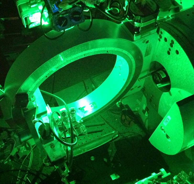 Photo - An optical laser interacts with a thin-film material in an experiment at SLAC's Stanford Synchrotron Radiation Lightsource. The circular instrument is part of an X-ray diffractometer.