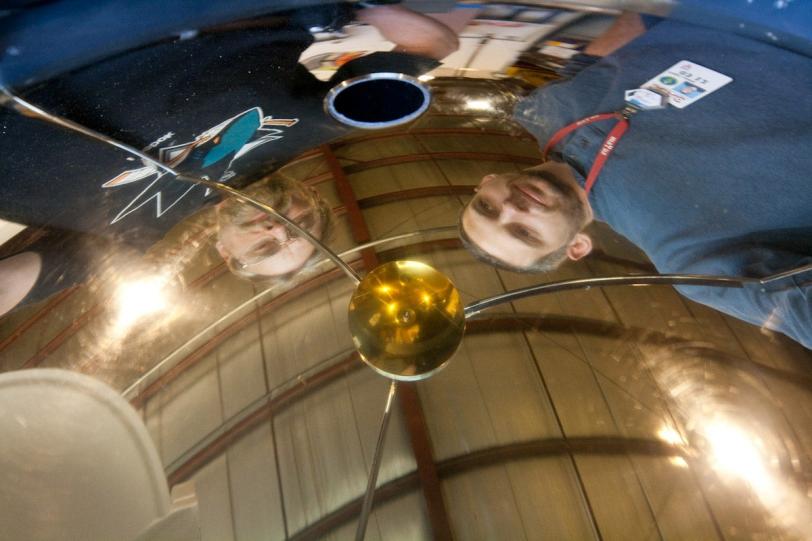 Team members Howard Rogers (left) and Peter Lewis (right) are reflected in the gold-coated hemispherical mirror of RASICAM – the Radiometric All Sky Infrared Camera. 