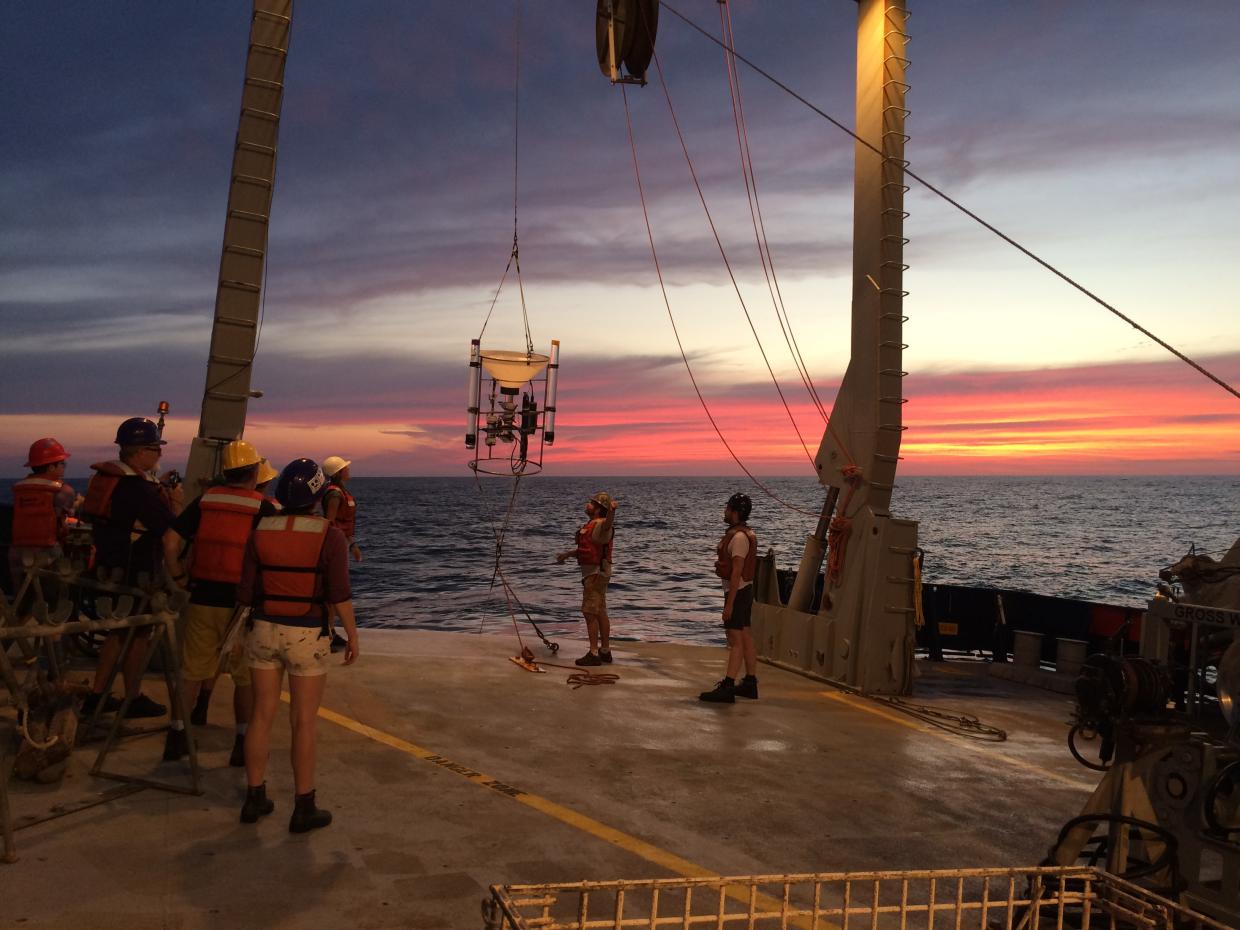 Scientists watch from a ship deck as a sample is hauled in from the ocean.